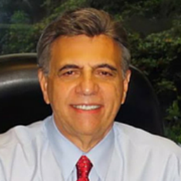 A man with a red tie sitting in front of trees. A man with a red tie sitting in front of trees.