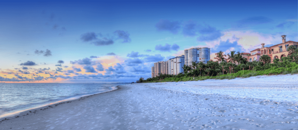 A beach with buildings in the background and clouds.
